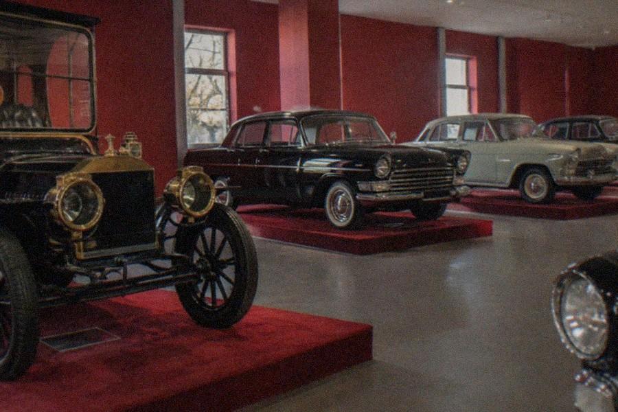A curved museum ramp lined with historic automobiles under bright ceiling lights
