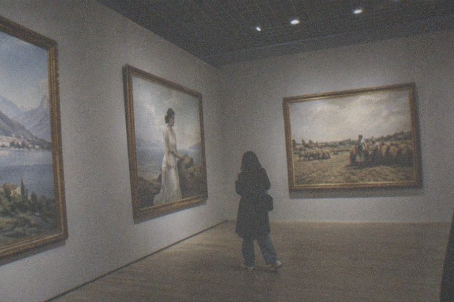 Visitors walking a long lane between gallery buildings on a sunny afternoon