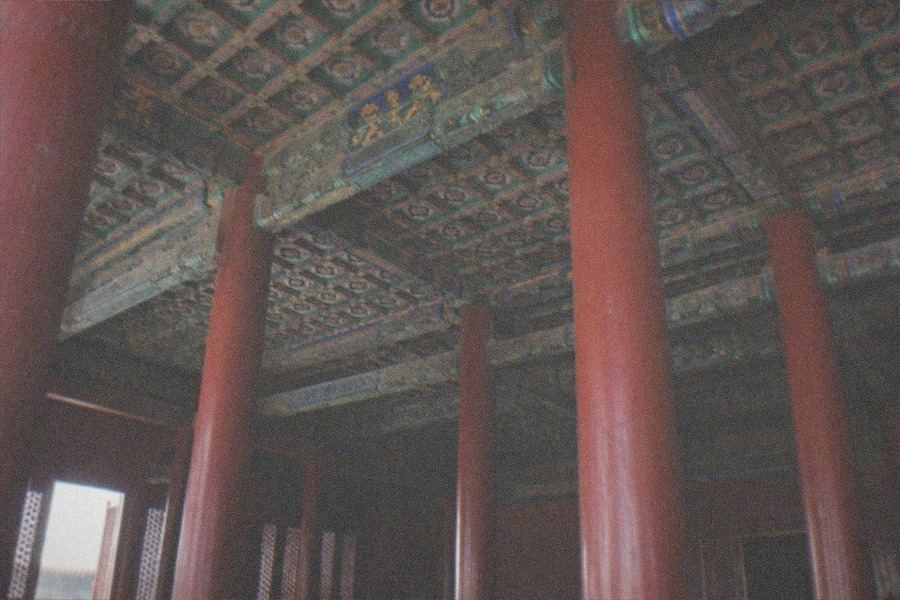 A stone gate and red walls of an imperial palace under a clear sky, seen from a plaza