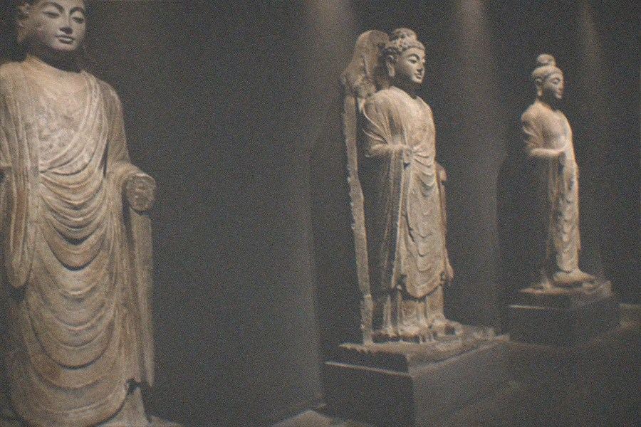 A carved Buddhist stone figure standing in a softly lit gallery on the upper floors of the Poly Art Museum
